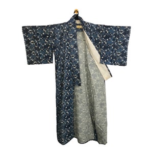 May include: A long, open-front kimono with a floral pattern in shades of blue and white. The kimono is hanging on a wooden hanger against a white background. The sleeves are wide and the interior lining is a light grey colour.