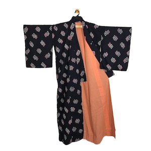 May include: A dark blue kimono with a geometric pattern of white and pink diamonds. The kimono is open, revealing a peach-coloured lining. The garment is hanging on a black hanger.