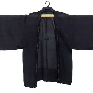Puede incluir: Un kimono negro con mangas largas y un diseño sencillo. El kimono está hecho de una tela ligera y tiene un corte holgado.