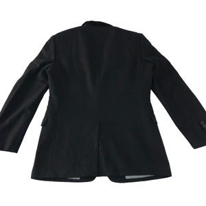 Puede incluir: Blazer negro con dise&ntilde;o cl&aacute;sico, visto desde atr&aacute;s. La chaqueta presenta solapa de muesca, dos bolsillos laterales y pu&ntilde;o con tres botones. El blazer est&aacute; confeccionado con una tela oscura y lisa.