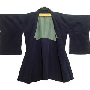 May include: A navy blue kimono jacket with wide sleeves, suspended from a black hanger. The interior lining is a light green hue. The jacket is open at the front, displaying the lining.