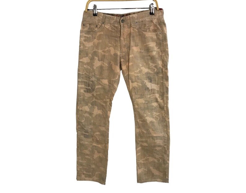 May include: A pair of camouflage-patterned jeans in a light brown color. The jeans have a straight leg and a relaxed fit.