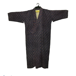May include: A dark-colored kimono-style robe with a repeating pattern of small red and blue shapes. The robe is hanging on a black hanger against a white background. The robe has long sleeves and a wrap-around design.