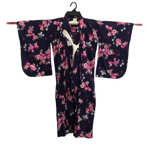 May include: A navy blue kimono, patterned with pink and white floral designs. The robe is displayed on a black hanger, featuring a white tie. The sleeves are wide, and the fabric suggests a lightweight material.