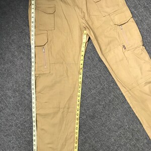 Pu&ograve; includere: Pantaloni cargo color cachi con pi&ugrave; tasche, tra cui alcune con cerniera. I pantaloni misurano circa 109 cm di lunghezza. I pantaloni hanno una chiusura con bottone e cerniera. Il tessuto sembra essere un materiale resistente e tessuto.