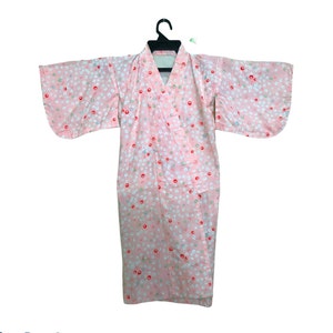 May include: A pink kimono with a white, red, and light blue polka dot pattern. The kimono is hanging on a black hanger against a white background. The sleeves are wide and the garment has a wrap-around design.