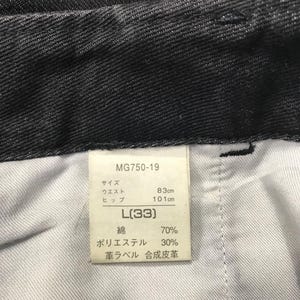 May include: Close-up of black denim trousers with a tag. The tag reads "MG750-19" and includes measurements: waist 83cm, hips 101cm, and size L(33). The fabric composition is 70% cotton and 30% polyester.