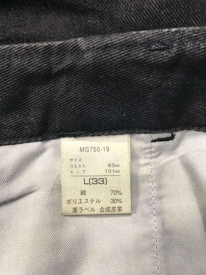 May include: Close-up of black denim trousers with a tag. The tag reads "MG750-19" and includes measurements: waist 83cm, hips 101cm, and size L(33). The fabric composition is 70% cotton and 30% polyester.