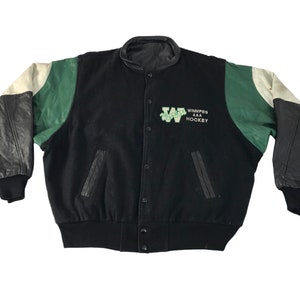 May include: Black varsity jacket with green and cream leather sleeves. The jacket has the text "Winnipeg AAA Hockey" in green on the chest. It features a button-up front and two front pockets. The cuffs and collar are black.