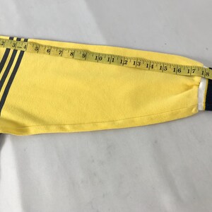 May include: A long-sleeved shirt with a navy blue body and a yellow sleeve. The yellow sleeve has three black stripes and a white and navy blue striped cuff. A measuring tape shows the sleeve is approximately 20 inches long.