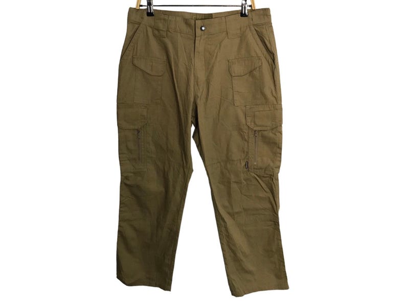 Pu&ograve; includere: Pantaloni cargo verde oliva con pi&ugrave; tasche e chiusura con zip laterale. I pantaloni sono appesi a una gruccia di legno. Questi pantaloni sono di stile casual.