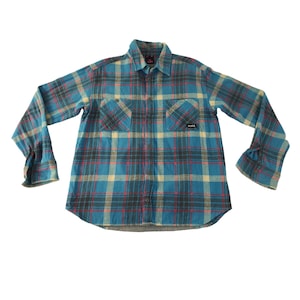 May include: A blue plaid flannel shirt with long sleeves, two chest pockets, and a button-down collar. The shirt features a pattern of blue, red, black, and beige squares. The brand name "jeans" is visible on a small black label on the left chest pocket.