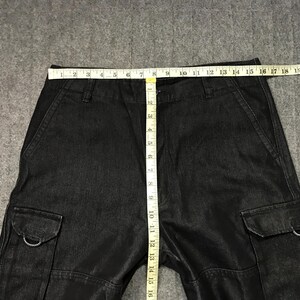 May include: Black denim cargo trousers with multiple pockets and a straight leg. A measuring tape shows the waist width. The trousers have a small red and white logo on the side.