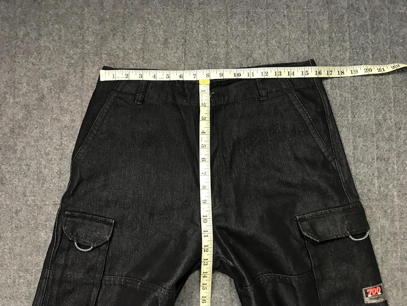 May include: Black denim cargo trousers with multiple pockets and a straight leg. A measuring tape shows the waist width. The trousers have a small red and white logo on the side.