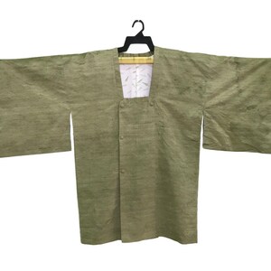 May include: A light green kimono-style robe with wide sleeves, hanging on a black hanger. The robe has a textured appearance and a button closure. The interior lining is white with a subtle pattern.