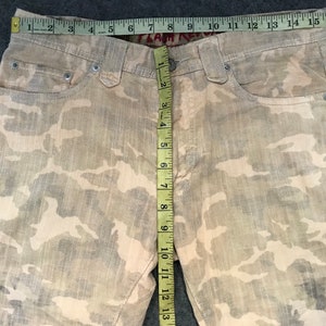 May include: A pair of beige camouflage print corduroy pants with a measuring tape showing the inseam is 33 inches.