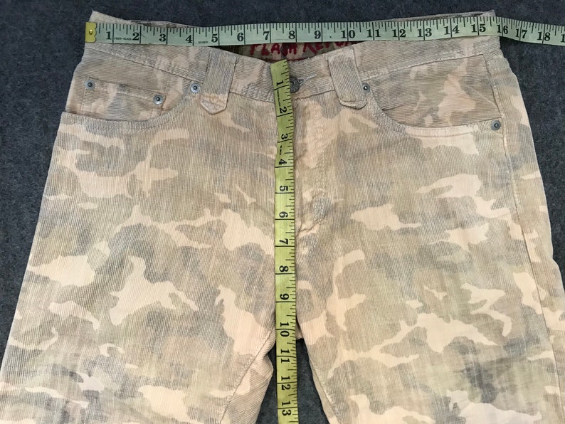 May include: A pair of beige camouflage print corduroy pants with a measuring tape showing the inseam is 33 inches.