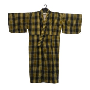May include: A long, plaid robe in black and gold hangs from a black hanger. The robe features a classic plaid pattern and a wrap-around design with wide sleeves. The robe is made of a soft, textured fabric.