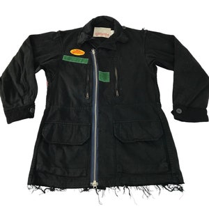 Peut inclure: Veste noire avec fermeture éclair, deux poches avant et ourlet effiloché. La veste a un col et des manches longues avec poignets boutonnés. Des écussons verts et oranges sont visibles sur la poitrine. La marque "siddartha" est sur l'étiquette.