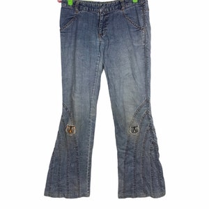 May include: Blue denim jeans with a flared leg design. The jeans feature decorative stitching and embroidered tiger patches near the knees. The jeans are hanging on a green hanger.