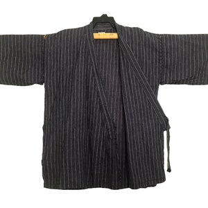 Könnte beinhalten: Ein dunkelgrau-weiß gestreifter Kimono-Stil-Bademantel. Der Bademantel hat lange Ärmel und ein Wickeldesign mit Krawattenverschluss. Der Stoff hat vertikale Streifen und hängt an einem Holzbügel.