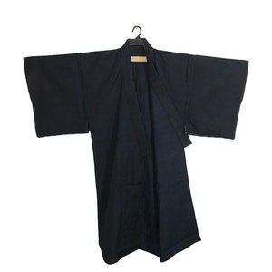 Puede incluir: Una bata kimono azul marino oscuro, colgada de una percha negra. La bata tiene mangas anchas y un diseño envolvente. La tela parece ser un material ligero, adecuado para usar en capas o como una prenda de abrigo.