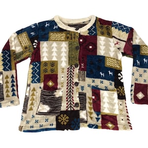 May include: A patchwork jacket with a cream-coloured collar and button closure. The jacket features a variety of patterned squares in shades of blue, burgundy, green, and cream, with tree, horse, and geometric designs. Two pockets are visible.