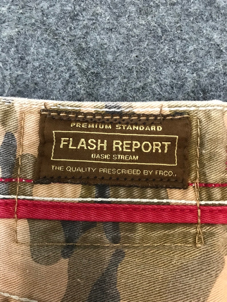 May include: A brown label with the text "Premium Standard Flash Report Basic Stream The Quality Prescribed by FRCO." on a camouflage fabric background.