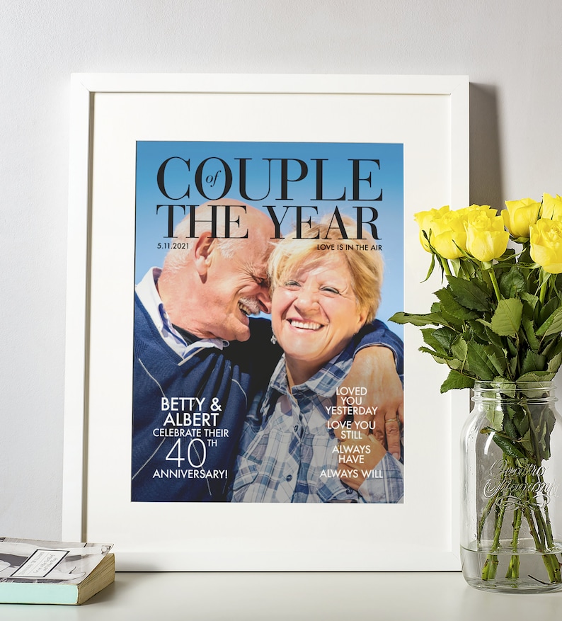May include: A framed photo of an older couple celebrating their 40th anniversary. The photo is in a magazine style layout with the text "Couple of the Year" and "Love is in the air". The couple is smiling and hugging. The text below the photo reads "Betty & Albert Celebrate their 40th Anniversary!" and "Loved you yesterday, love you still, always have, always will."