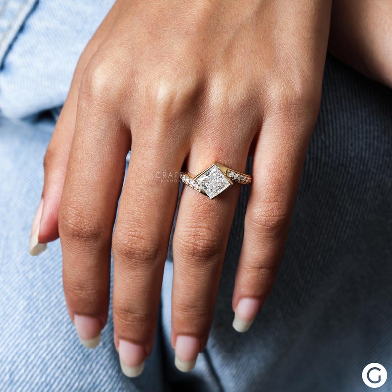 May include: A gold ring with a large square-shaped diamond set in the center. The band is adorned with smaller diamonds that create a sparkling effect.