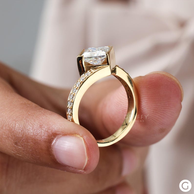 May include: A gold engagement ring with a large, square-shaped diamond set in a unique, angled setting. The band is adorned with smaller diamonds.