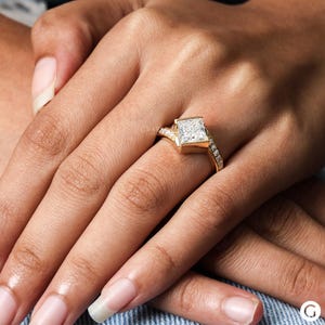 May include: A gold engagement ring with a large square-shaped diamond and smaller diamonds set in the band.