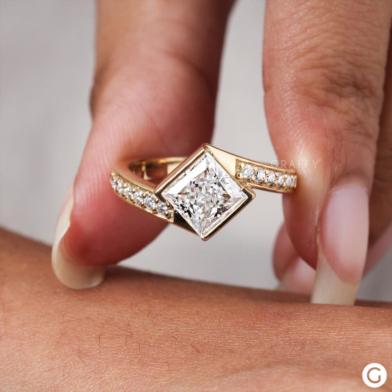 May include: A gold engagement ring with a square-shaped diamond set in a unique, angled setting. The band is adorned with smaller diamonds.