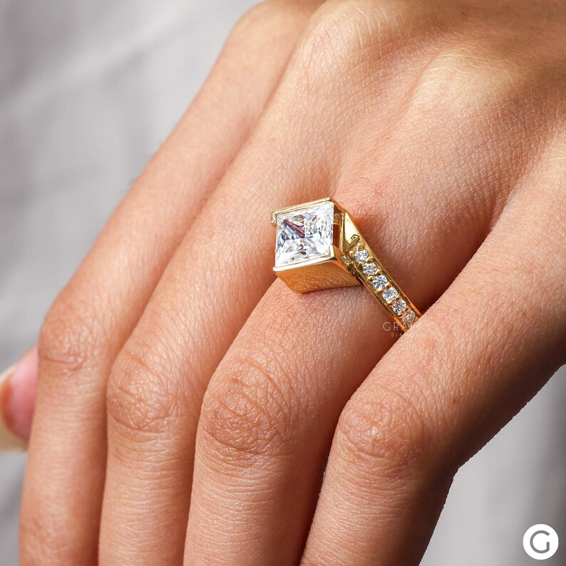 May include: A gold engagement ring with a square-shaped diamond and a band of smaller diamonds.