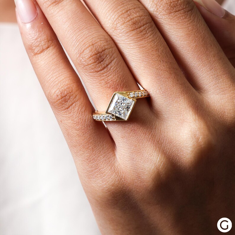 May include: A gold ring with a large, square-shaped diamond set in a prong setting. The ring has a twisted band with smaller diamonds set along the band.