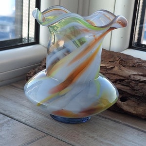 Könnte beinhalten: Eine weiße Glasvase mit orangefarbenen, gelben und grünen Wirbeln. Die Vase hat einen breiten Boden und einen schmalen Hals mit einem gekräuselten oberen Rand.