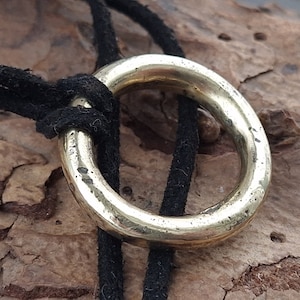May include: A gold-colored metal ring pendant on a black leather cord. The ring is thick and has a smooth, rounded surface.