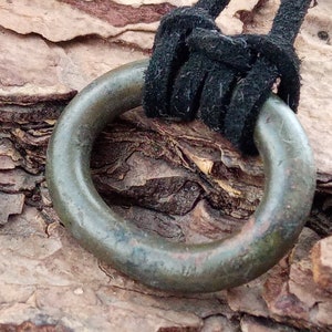 Op de afbeelding: Een grote, ronde, groene metalen ringhanger met een zwart koord eraan bevestigd. De hanger heeft een glad, versleten oppervlak en hangt aan een stuk boomschors.