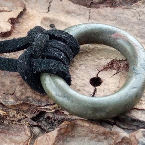 Op de afbeelding: Een groene metalen ring hanger met een zwart leren koord. De ring is glad en heeft een verweerde uitstraling.