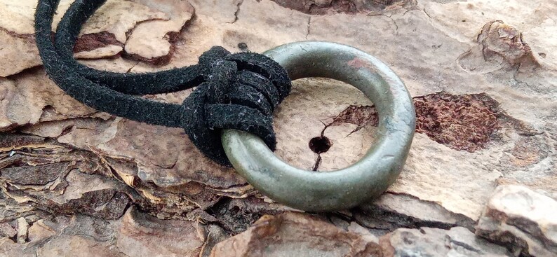 Op de afbeelding: Een groene metalen ring hanger met een zwart leren koord. De ring is glad en heeft een verweerde uitstraling.