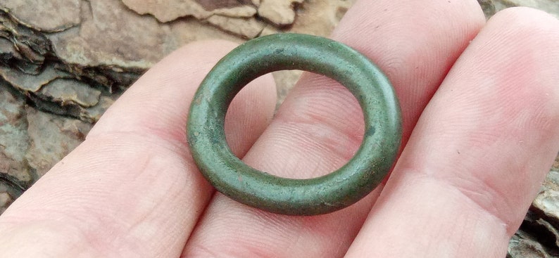 Op de afbeelding: Een groene metalen ring met een glad, afgerond oppervlak.