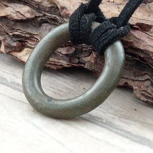 Op de afbeelding: Een donkergroene metalen ringhanger aan een zwart leren koord. De hanger is een eenvoudige cirkel met een glad oppervlak.