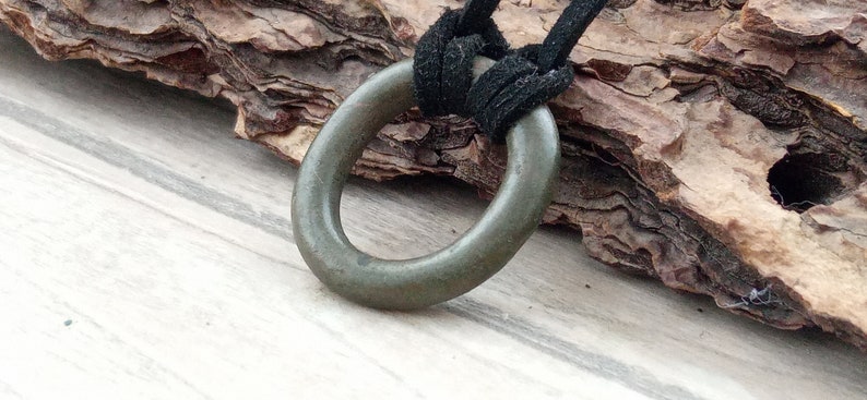 Op de afbeelding: Een donkergroene metalen ringhanger aan een zwart leren koord. De hanger is een eenvoudige cirkel met een glad oppervlak.