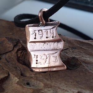 May include: A copper pendant necklace with a rectangular shape and a textured surface. The pendant has an inscription that reads "1914".