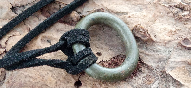 Op de afbeelding: Een groene metalen ring met een zwart koord erdoorheen geregen. De ring is met een knoop aan het koord vastgemaakt.