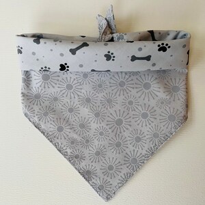 May include: A gray dog bandana with a black paw print and bone pattern on the top and a gray starburst pattern on the bottom.