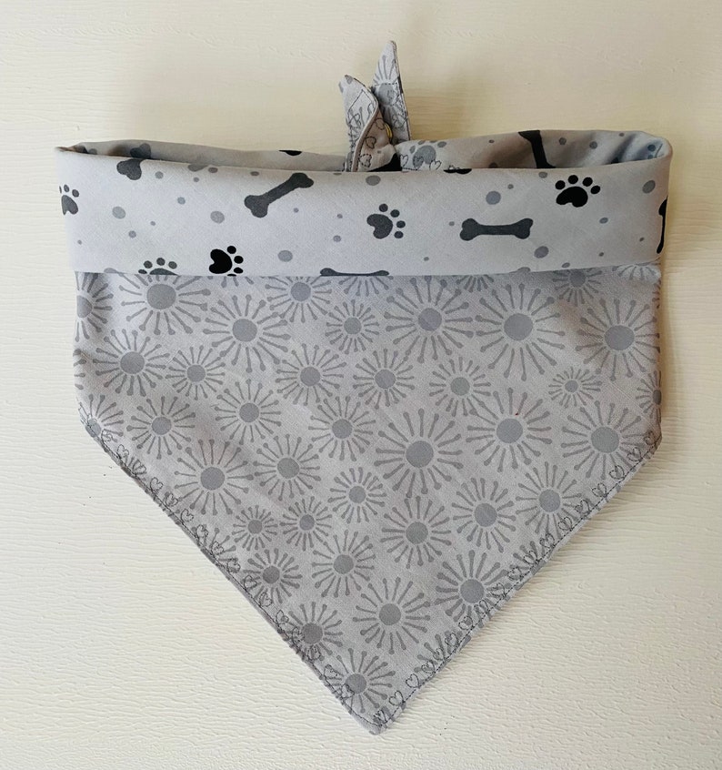 May include: A gray dog bandana with a black paw print and bone pattern on the top and a gray starburst pattern on the bottom.