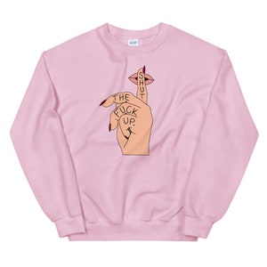 May include: Pink sweatshirt with a graphic of a hand with a finger over its mouth, with the text "SHUT THE FUCK UP."