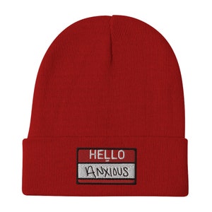 May include: Red knit beanie with a white name tag that says "HELLO ANXIOUS" in a handwritten style.