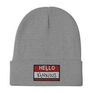 May include: Gray knitted beanie with a red and white name tag that reads "HELLO ANXIOUS".